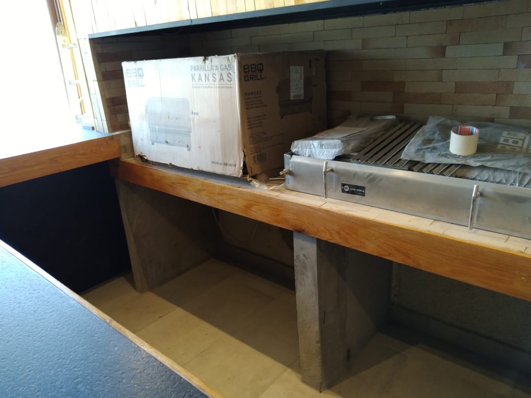 Cocina exterior de quincho de 70 m², mesón en piedra y equipamiento de parrilla